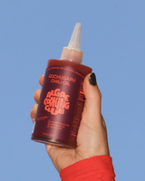 Hand holding a bottle of Algae Cooking Club's Gochugaru Chili Oil against a blue sky.