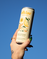 Hand holding a can of Allldae Ginger Yuzu Superfruit Soda against a clear blue sky.
