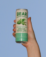 Hand holding a can of Bear Maple Farms Sparkling Ginseng Tonic in Lemongrass Mint against a blue sky.