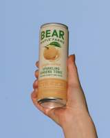 Hand holding a can of Bear Maple Farms Sparkling Ginseng Tonic in Yuzu Citrus against a blue sky.