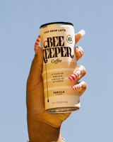Hand holding a can of Bee Keeper Coffee Cold Brew Latte in Vanilla against a blue sky.