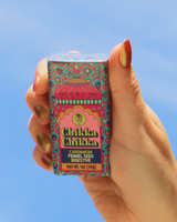 Hand holding a colorful box of Chikka Chikka cardamom fennel seed digestive against a blue sky background