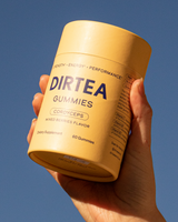 Hand holding a container of DIRTEA Cordyceps Gummies against a blue sky