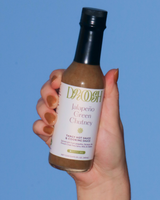 Hand holding a bottle of Dosh Jalapeño Green Chutney against a blue sky