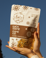 Hand holding a package of Eve's Black Sesame crackers against a blue sky.