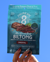 Package of Figure 8 Air-Dried Beef Biltong held by a hand against a blue background