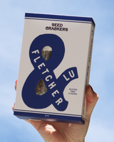 Hand holding a box of Fletcher & Lu Plain Seed Crackers against an open sky.