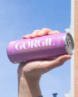 Hand holding a can of Gorgie Electric Berry Sparkling Energy Drink can against a clear blue sky.