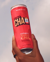 Hand holding a can of House of Cha's Oatmilk Masala Cha against a cloudy sky.