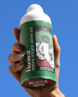 Hand holding a bottle of Huwa Extra Virgin Olive Oil against an open sky.