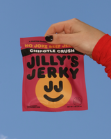 Hand holding a package of Jilly's Jerky Chipotle Crush flavor against a blue sky.