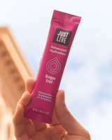 Pink 'Just Live' hydration packet with dragon fruit flavor held in a hand against a blurred background