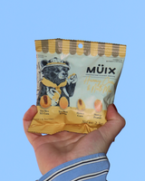 Hand holding a package of Muix Hunny Corn & Nuts mix against an open sky.