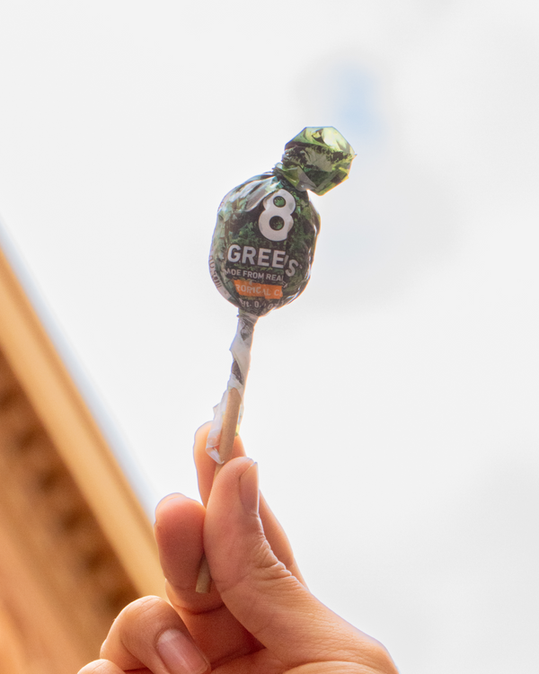 Hand holding a 8 Greens Tropical Citrus Lollipop against a clear sky. 