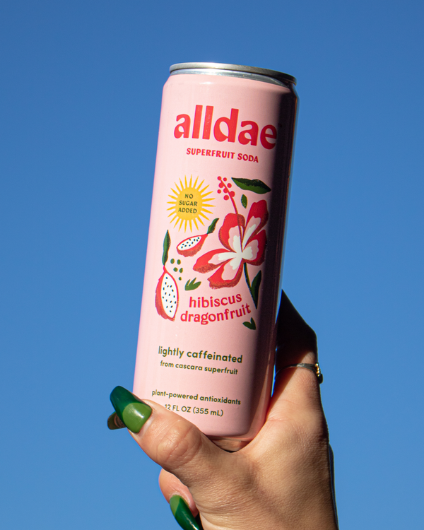 Hand holding a can of Alldae Hibiscus Dragonfruit Superfruit Soda against a blue sky. 