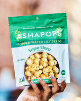 Hand holding a package of Ashapops Vegan Cheese flavored popped water lily seeds.