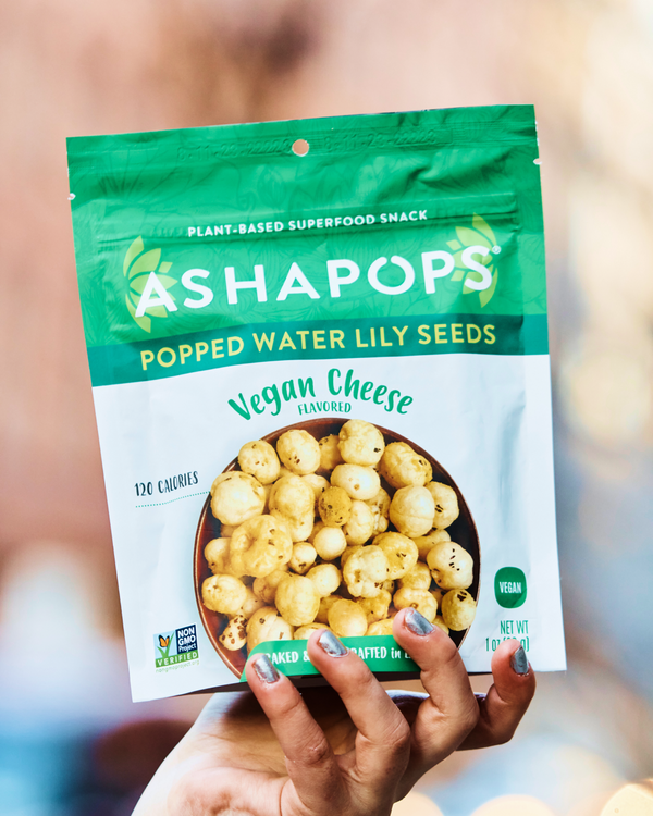 Hand holding a package of Ashapops Vegan Cheese flavored popped water lily seeds.
