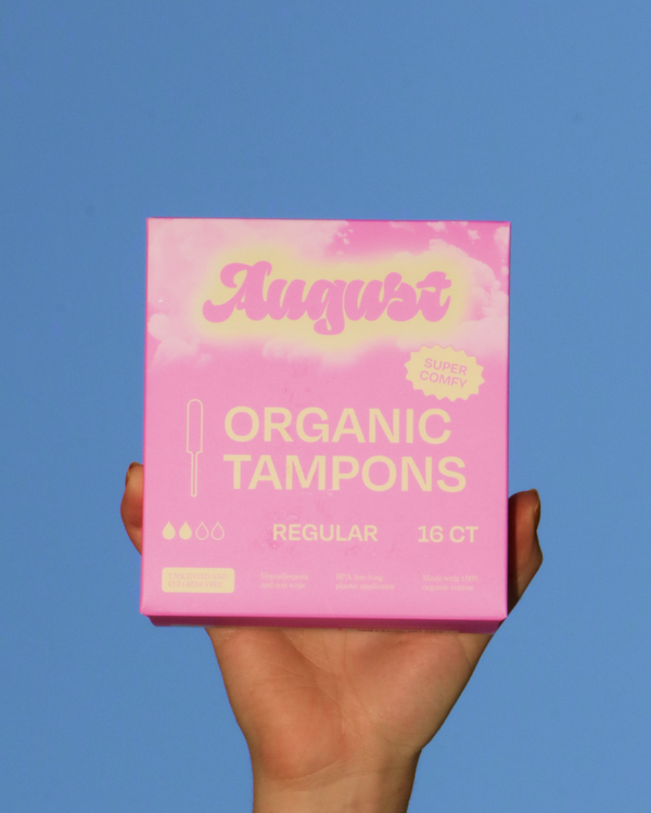Hand holding a box of August Organic Tampons against a blue sky. 