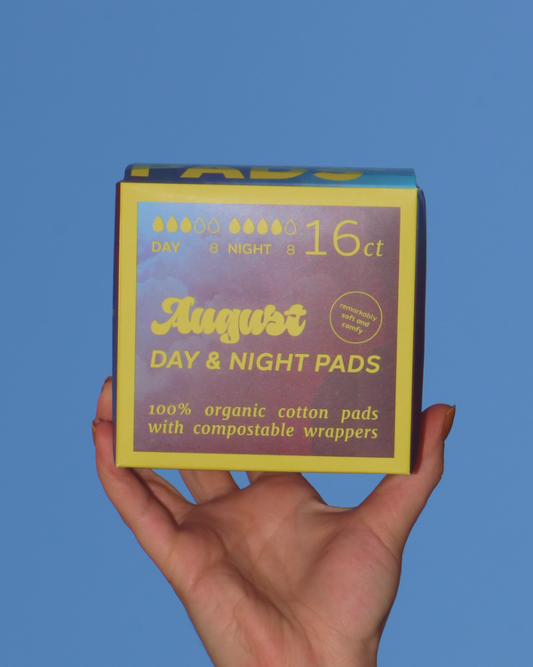 Hand holding a box of August Day & Night Pads against a blue sky.