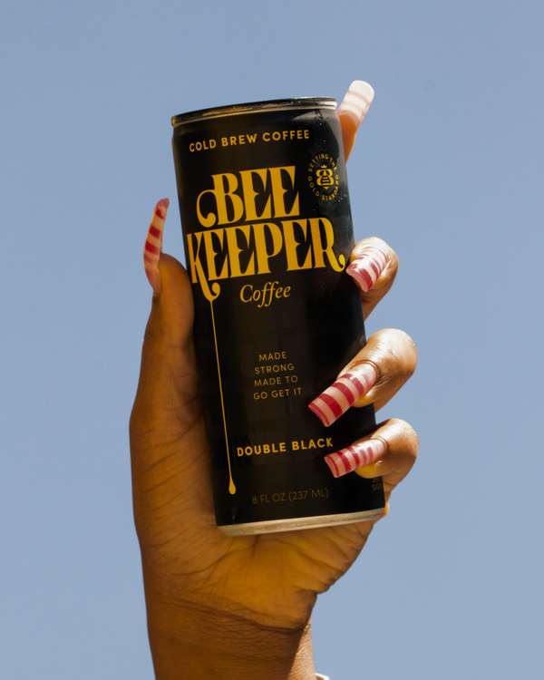 Hand holding a can of Beekeeper Coffee in Double Black against a clear blue sky.