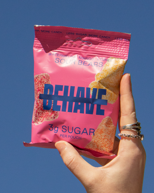 Hand holding a bag of Behave Sour Bears against a blue sky.