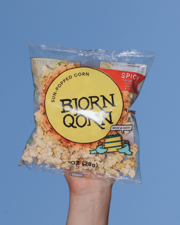 Small bag of Bjorn Qorn's Spicy popcorn held against a sky. 