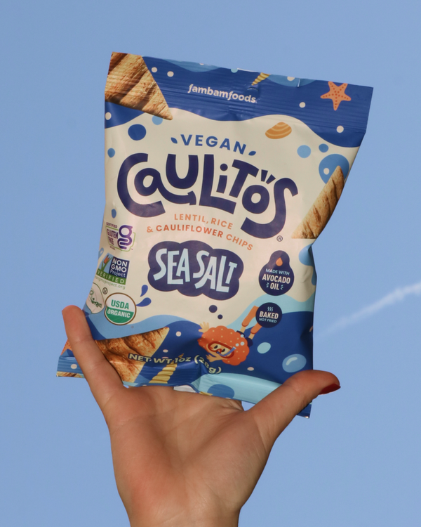 Hand holding a package of Vegan Caulitos Sea Salt chips against a blue sky.