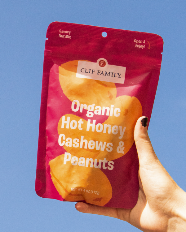 Hand holding a Clif Family Farms Organic Hot Honey Cashews and Peanuts against a blue sky