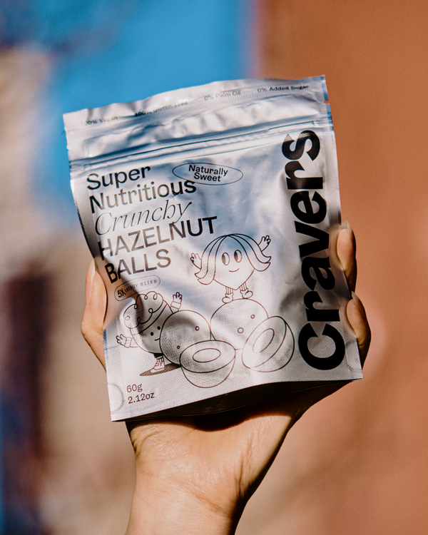 Hand holding a package of 'Cravers' Super Nutritious Crunchy Hazelnut Balls.