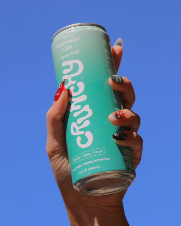 Hand holding a can of Crunchy Hydration's Watermelon Calm against a blue sky. 