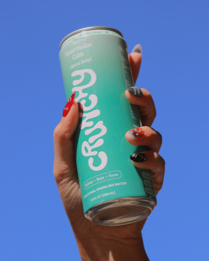 Hand holding a can of Crunchy Hydration's Watermelon Calm against a blue sky. 