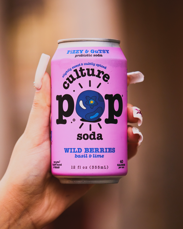 Hand holding a can of Culture Pop's Wild Berries, Basil & Lime soda against a blurred background. 
