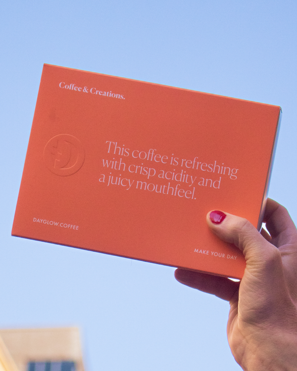 Hand holding a box of Dayglow Coffee Beans with juicy flavor notes. 
