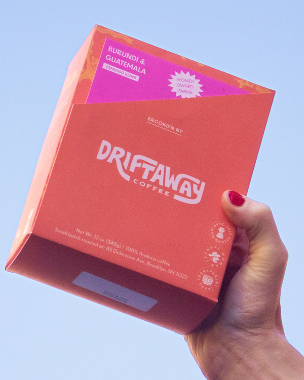 Hand holding a box of Driftaway Coffee Espresso Whole Bean Blend against a blue sky. 