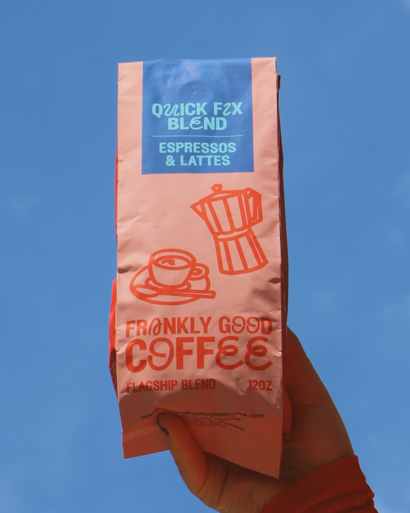 Hand holding a bag of Frankly Good Coffee's Quick Fix Blend against an open sky.