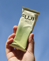 Hand holding a Fuji Matcha Protein Bar against an open sky.