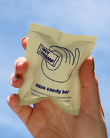 Hand holding a package of Hey Champ's Miso Candy Bar against an open sky.