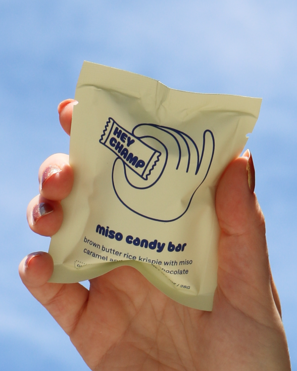 Hand holding a package of Hey Champ's Miso Candy Bar against an open sky.