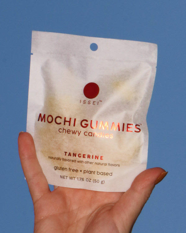 Hand holding a bag of Issei Tangerine Mochi Gummies against an open sky.
