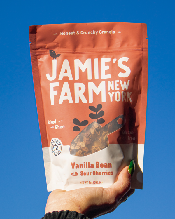 Hand holding a bag of Jamie's Farm Vanilla Bean with Sour Cherries Granola against an open sky.
