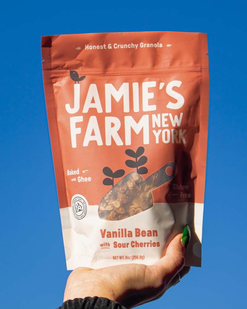 Hand holding a bag of Jamie's Farm Vanilla Bean with Sour Cherries Granola against an open sky.