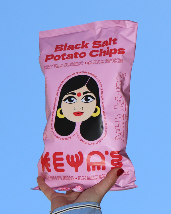 Hand holding a bag of Keya's Black Salt Potato Chips against an open sky.
