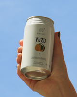 Hand holding a can of Kimino Yuzu sparkling water against a clear blue sky