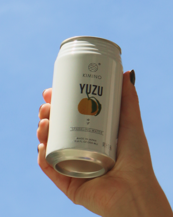 Hand holding a can of Kimino Yuzu sparkling water against a clear blue sky