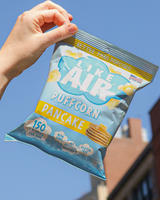 Hand holding a bag of Like Air Puffcorn Pancake flavor against a clear blue sky.