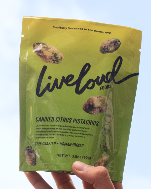 Hand holding a bag of Live Loud Food's Candied Citrus Pistachios against an open sky.