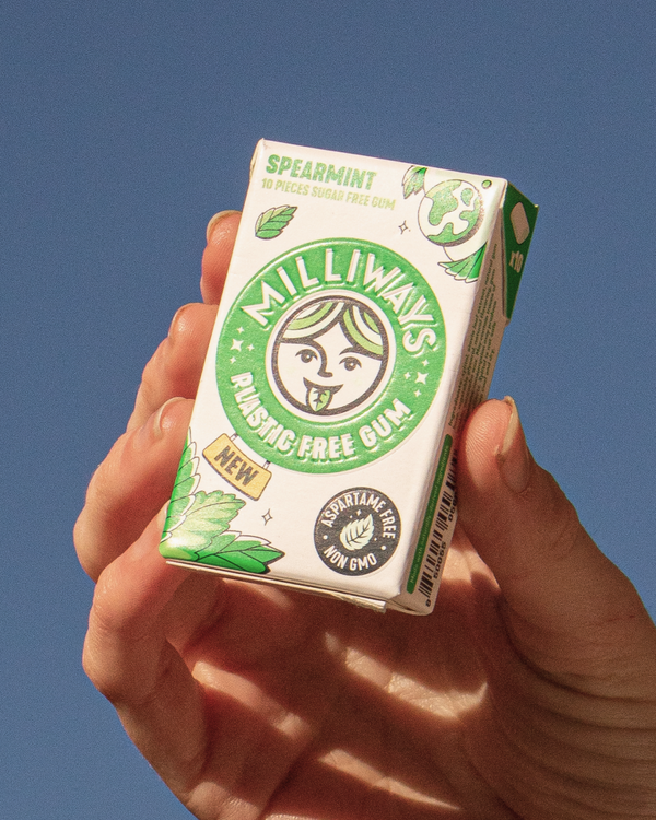 Hand holding a box of Milliways Plastic Free Spearmint gum against a blue sky.