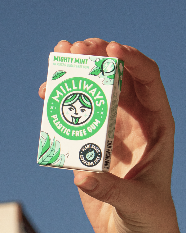 Hand holding a box of Milliways Might Mint Plastic Free Gum against a blue sky.