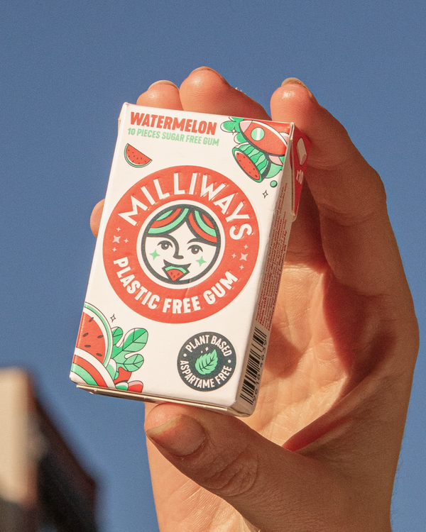 Hand holding a box of Milliways Plastic Free Gum against a cityscape. 