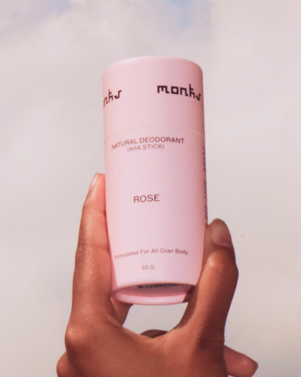 Hand holding a tube of Monk's Rose Natural Deodorant against a cloudy sky.